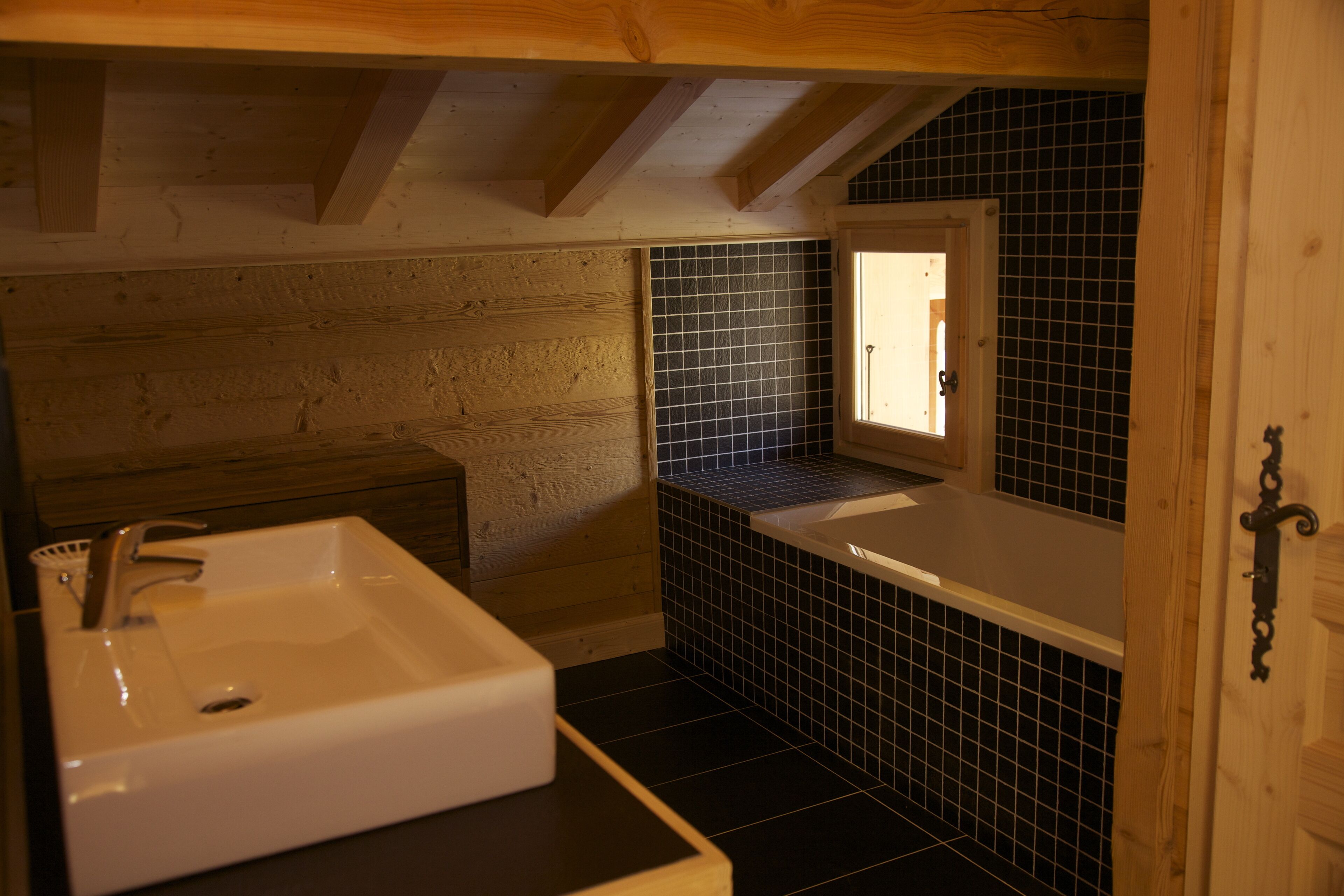 A small, compact bathroom with a white sink, a bathtub, and a window providing natural light.