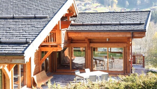 Eine Holzhütte mit geneigtem Dach, einer überdachten Veranda mit Sitzgelegenheiten und Blick auf eine gebirgige Landschaft.