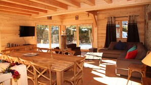 Ein Holzblock-Innenraum mit Essbereich, einer Couch und großen Fenstern.