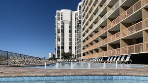 Une piscine à l’eau claire, entourée de chaises longues et bordée d’un bâtiment doté de nombreux balcons.