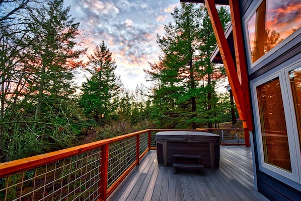 Terraza de madera con un jacuzzi, rodeada de árboles altos y una barandilla.