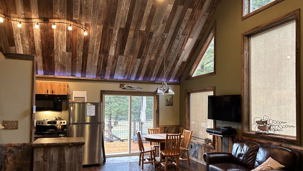 A rustic interior with a wooden ceiling, a dining area, a leather sofa, and a kitchen with stainless steel appliances. - Welcome to our Rock Creek Fortress of Solitude. (Philipsburg)