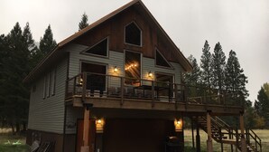 A two-story wooden house with a balcony, a garage, and a staircase leading to the upper level. - Welcome to our Rock Creek Fortress of Solitude. (Philipsburg)