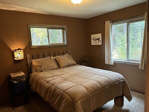 A bedroom with a bed, a nightstand, a window, and a wall-mounted light fixture.