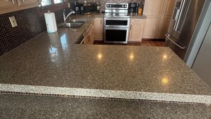 Cocina con encimeras de granito, electrodomésticos de acero inoxidable, armarios de madera y una isla grande con taburetes.