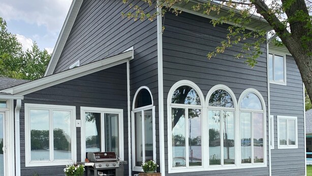 Una casa moderna de dos pisos con fachada gris oscuro, detalles blancos y grandes ventanales arqueados.