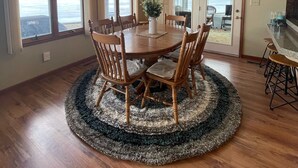 Comedor con mesa y sillas de madera, una araña y ventanas grandes con vista a un cuerpo de agua.