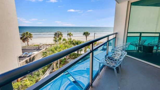 A balcony with a glass railing overlooking a beach.