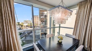 A hotel room with a large window, a dark wooden table with four chairs, a chandelier, and a vase with flowers.