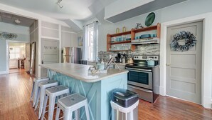 Una cocina con una isla central, taburetes de bar, un refrigerador, un horno y un fregadero.