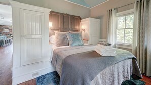 Un dormitorio con una cama grande, un aparador, una ventana con cortinas y vistas al exterior.