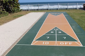 Een jeu de boules baan met cijfers en een 'UIT' gebied, naast een strand en een witte omheining.