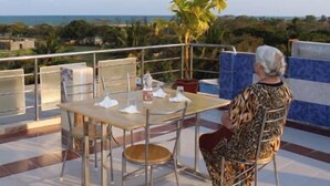 A terrace with a table and chairs, overlooking a coastal landscape with palm trees and a view of the sea. - Suradeep Residency (Tirukalukundram)
