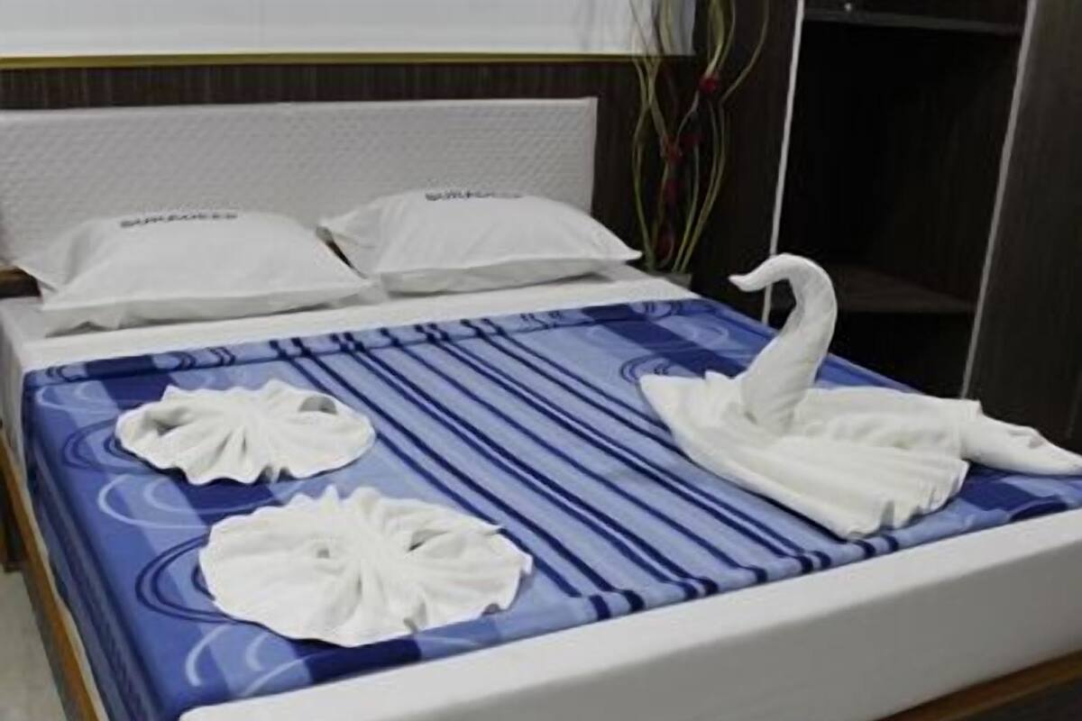A hotel room with a bed featuring a blue and white striped bedspread, two white pillows, and two white towels arranged on the bed.