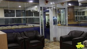 A room with two dark leather sofas, a wooden coffee table, and a patterned floor. - Suradeep Residency (Tirukalukundram)