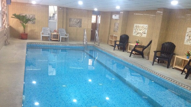 An indoor swimming pool with a tiled floor, surrounded by chairs and a potted plant. - Suradeep Residency (Tirukalukundram)