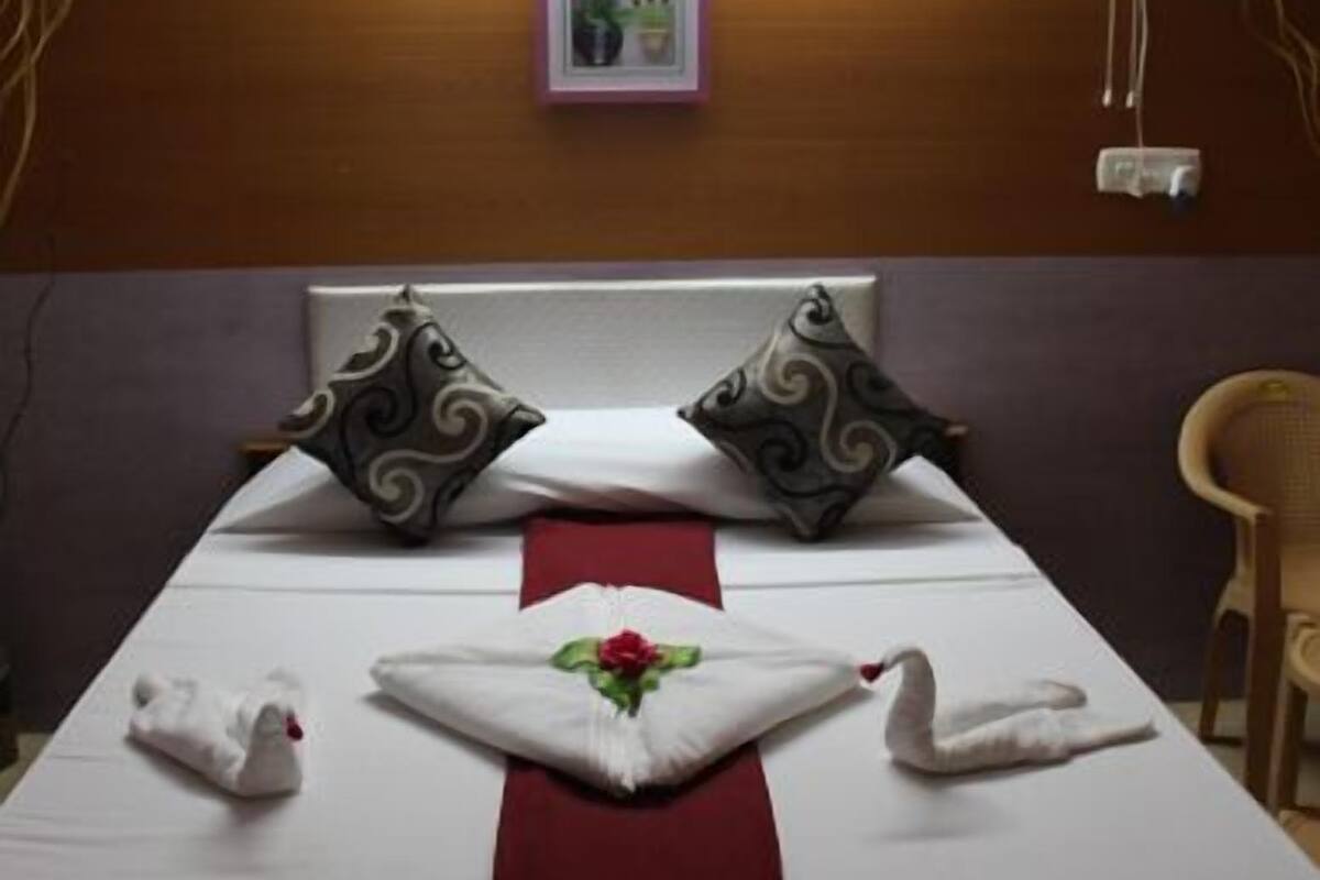 A neatly made bed with decorative pillows, a red bed runner, and swan-shaped towels.