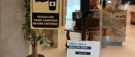 A hand sanitizer dispenser and a sign instructing to use it before entering.