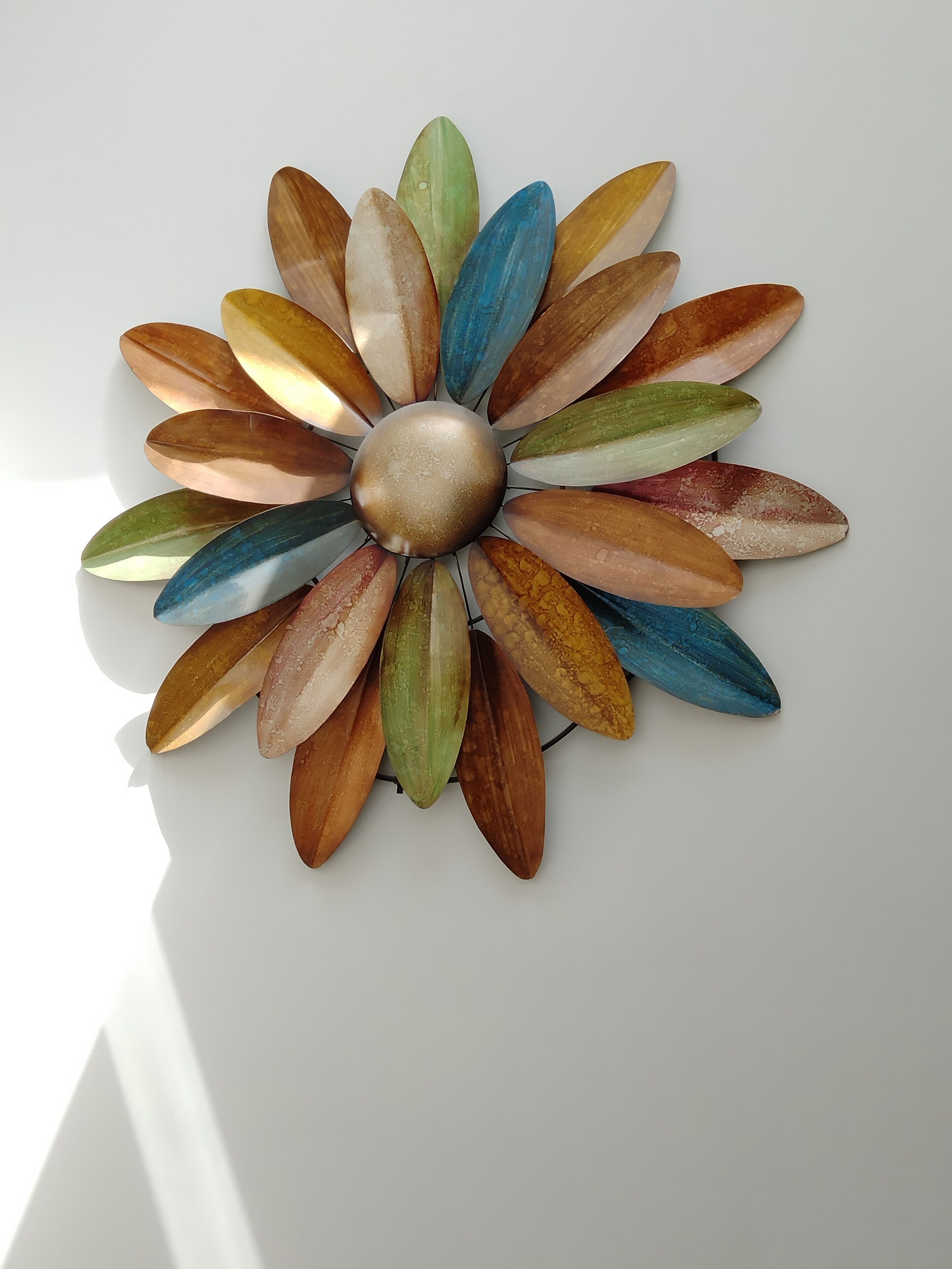 A wall-mounted decorative piece with a central metallic sphere surrounded by leaf-shaped elements in various colors.