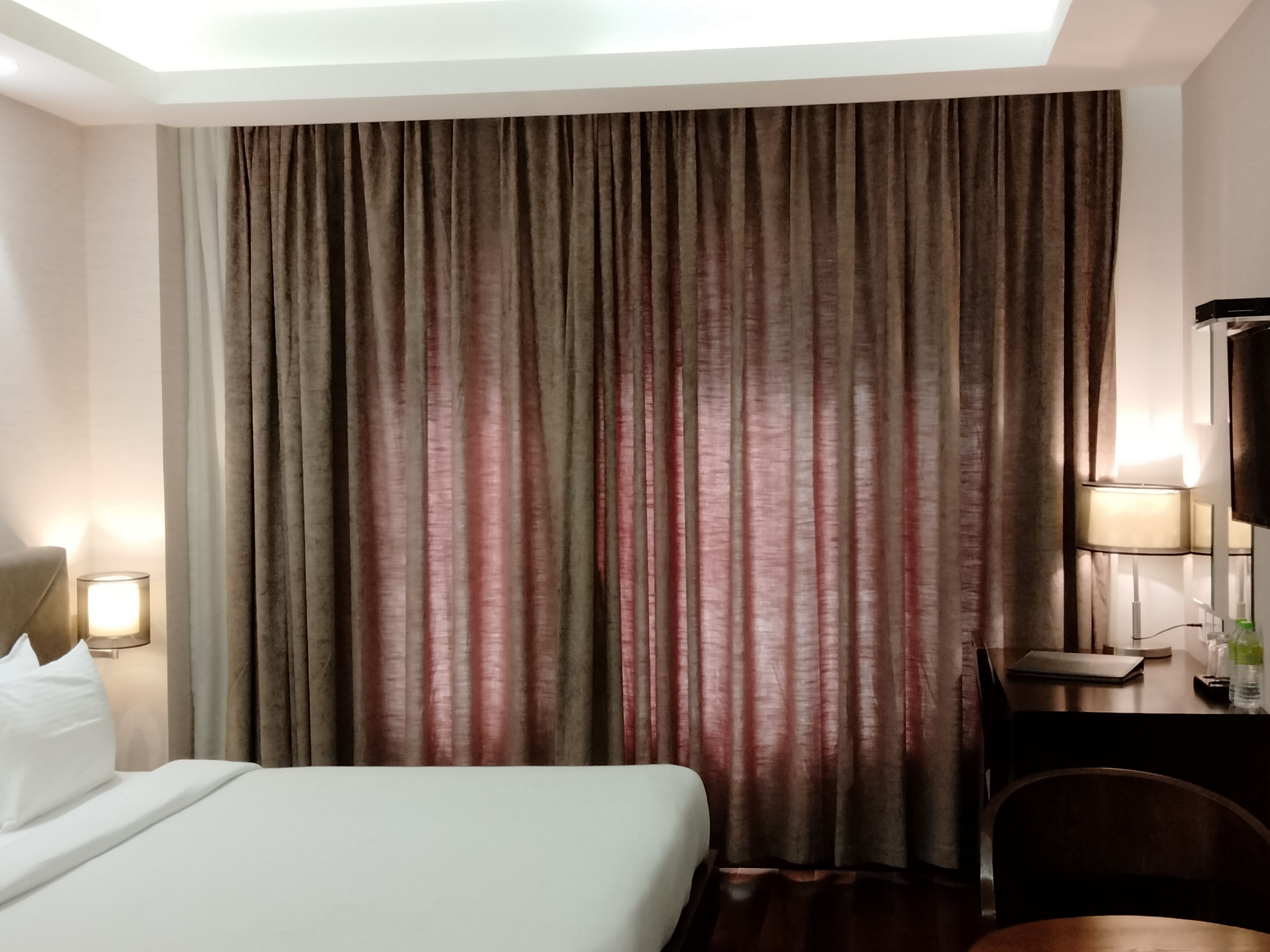 Hotellihuone, jossa on suuri sänky, työpöytä lampun kanssa ja televisio.