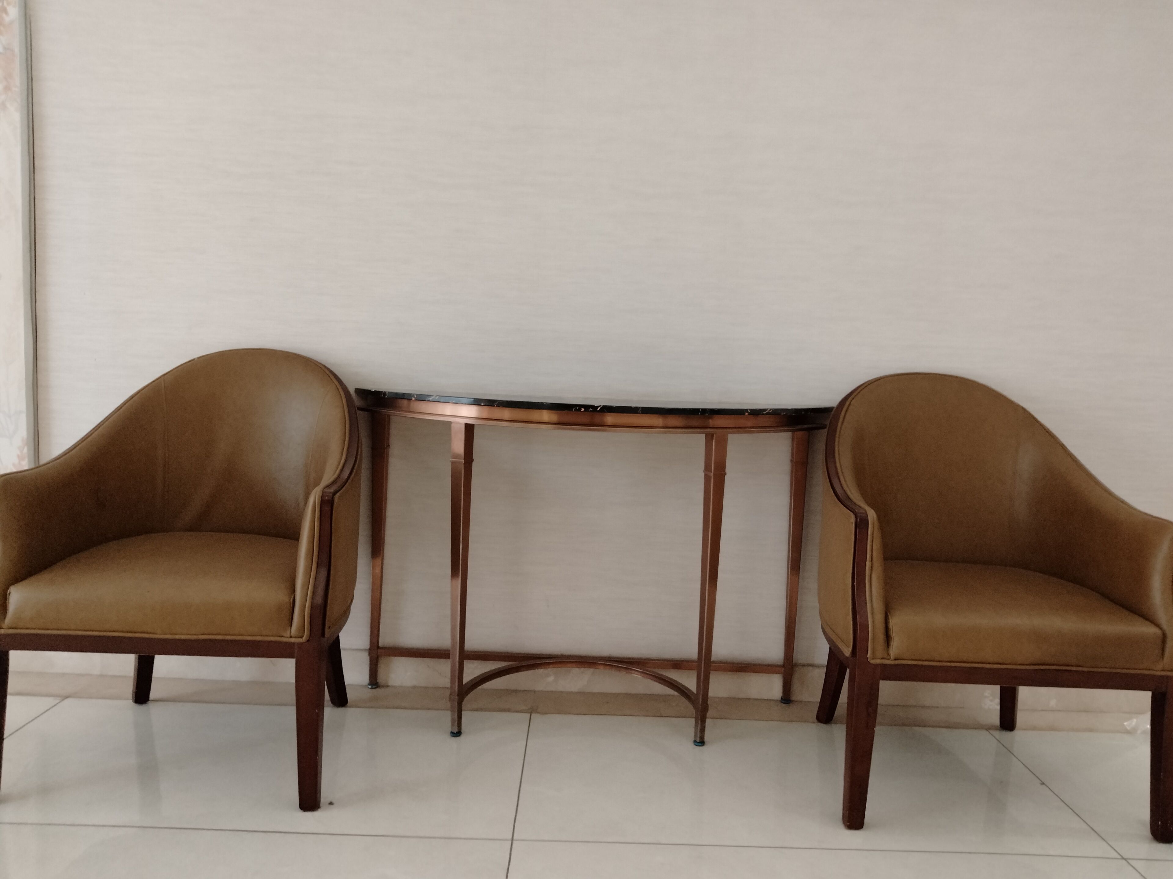 A room with two brown leather chairs and a round table with metal legs.