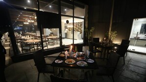 An outdoor dining area with tables and chairs, a view of the interior restaurant, and potted plants. - The Hamuse Hotel Kodaikanal - Luxury Redefined (Kodaikanal)