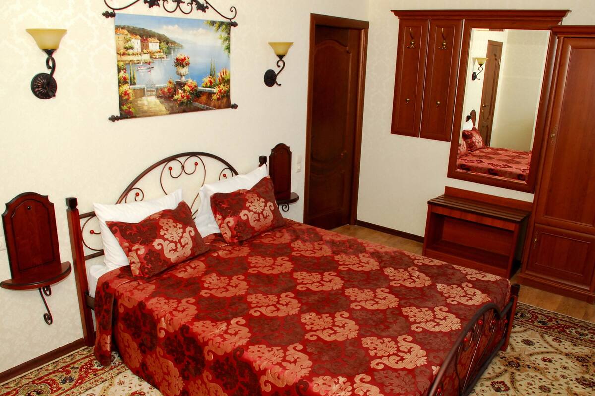 Quarto com cama, guarda-roupa de madeira, espelho e um quadro na parede.