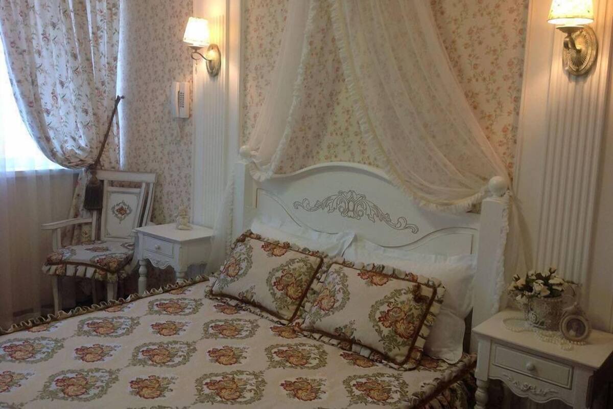 Quarto com cama de dossel, papel de parede floral e duas luminárias de cabeceira.