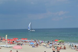 Una playa con tumbonas y sombrillas, un velero a lo lejos y un cielo despejado.