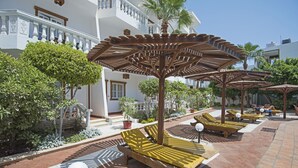 Un resort con áreas de estar al aire libre, palmeras y un edificio blanco con balcones.