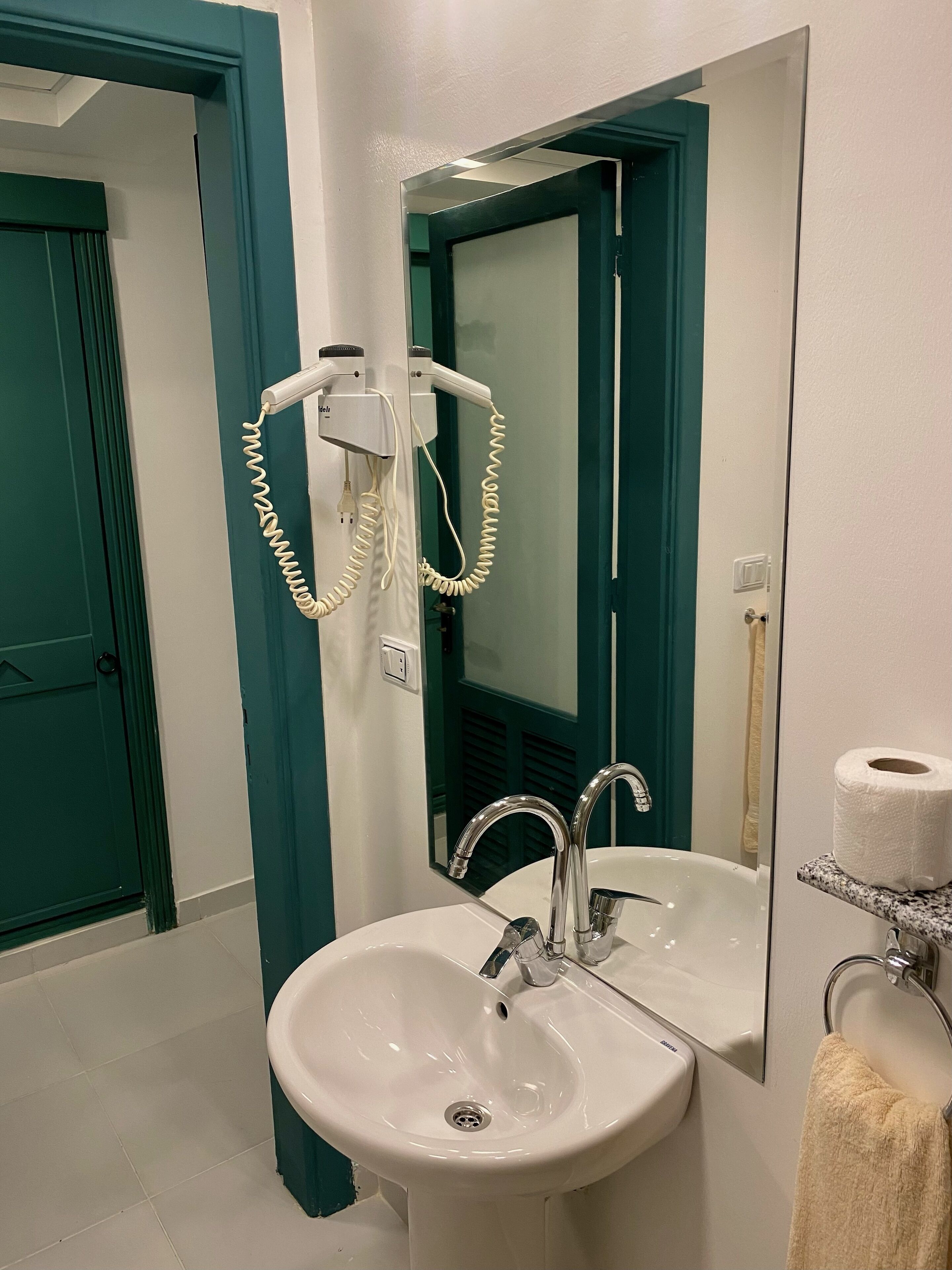 A bathroom with a white sink, a mirror, a towel rack, and a toilet paper holder.