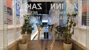Un moderno vestíbulo de hotel con entrada de vidrio, plantas en macetas y una escultura reflectante en el centro.