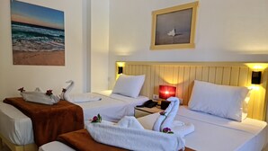 Habitación de hotel con dos camas, cada una con una manta marrón y toallas blancas dispuestas en forma de cisne. En la pared, un cuadro con una playa, y arriba de las camas, una foto enmarcada de un cisne.