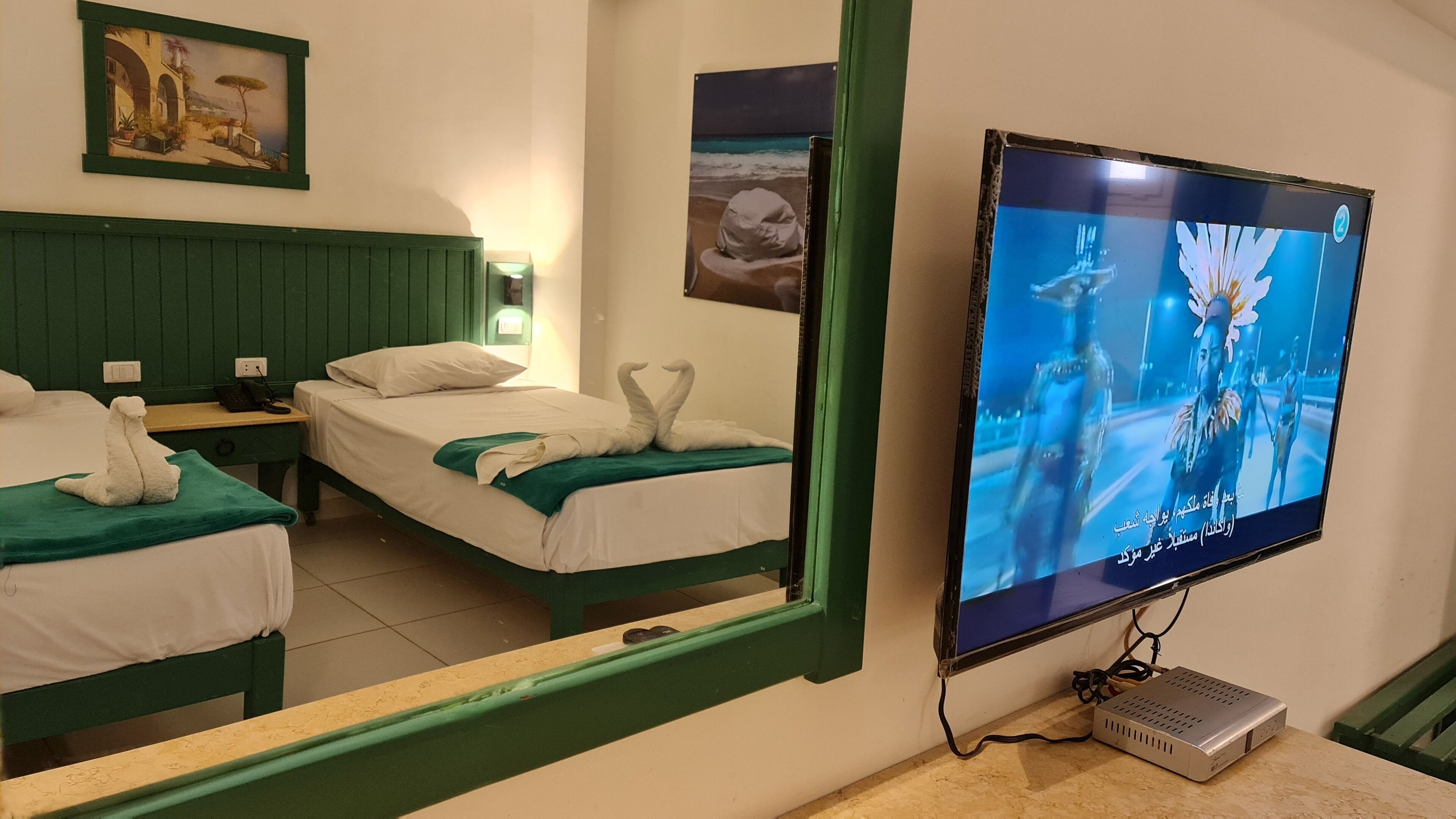 Camera d'albergo con due letti, una televisione montata a parete e uno specchio che riflette l'ambiente.