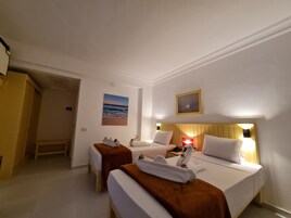 Una camera d'albergo con due letti singoli, una testiera in legno, un comodino, una lampada e un quadro raffigurante una spiaggia.