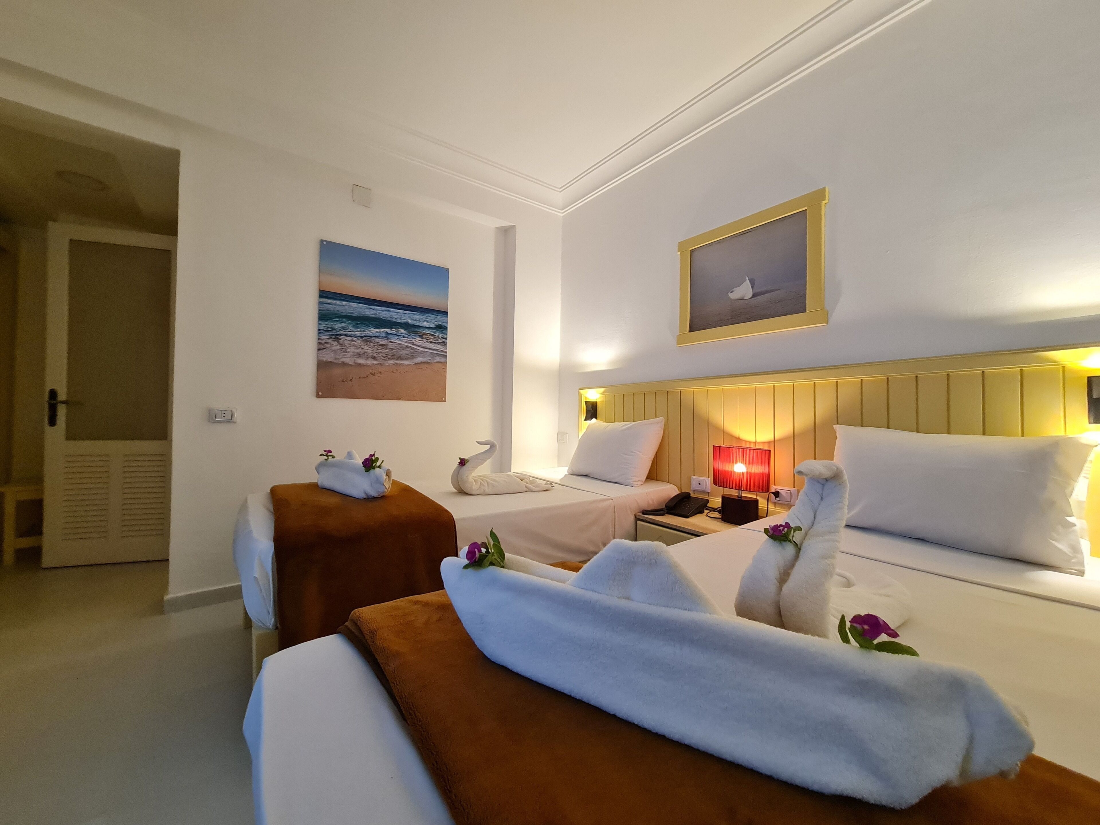 A hotel room with two beds, a nightstand, a lamp, and a painting of a beach scene.