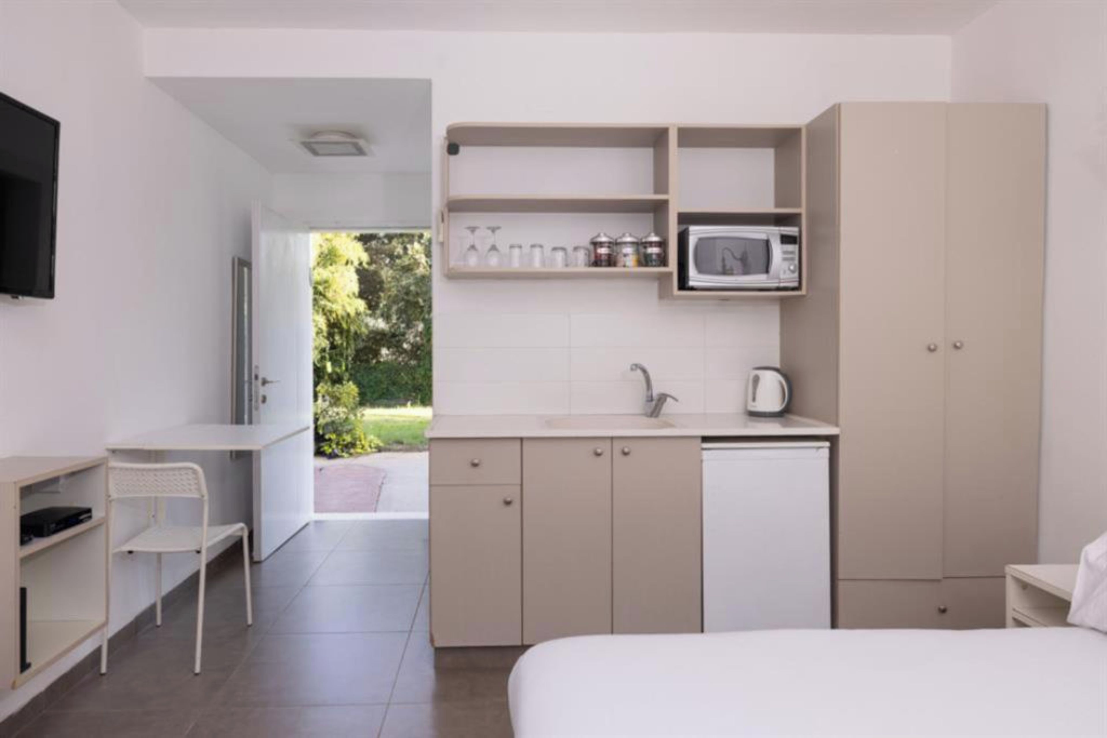Una camera d'albergo moderna e minimalista con un letto, una scrivania, angolo cottura e vista sull'esterno.