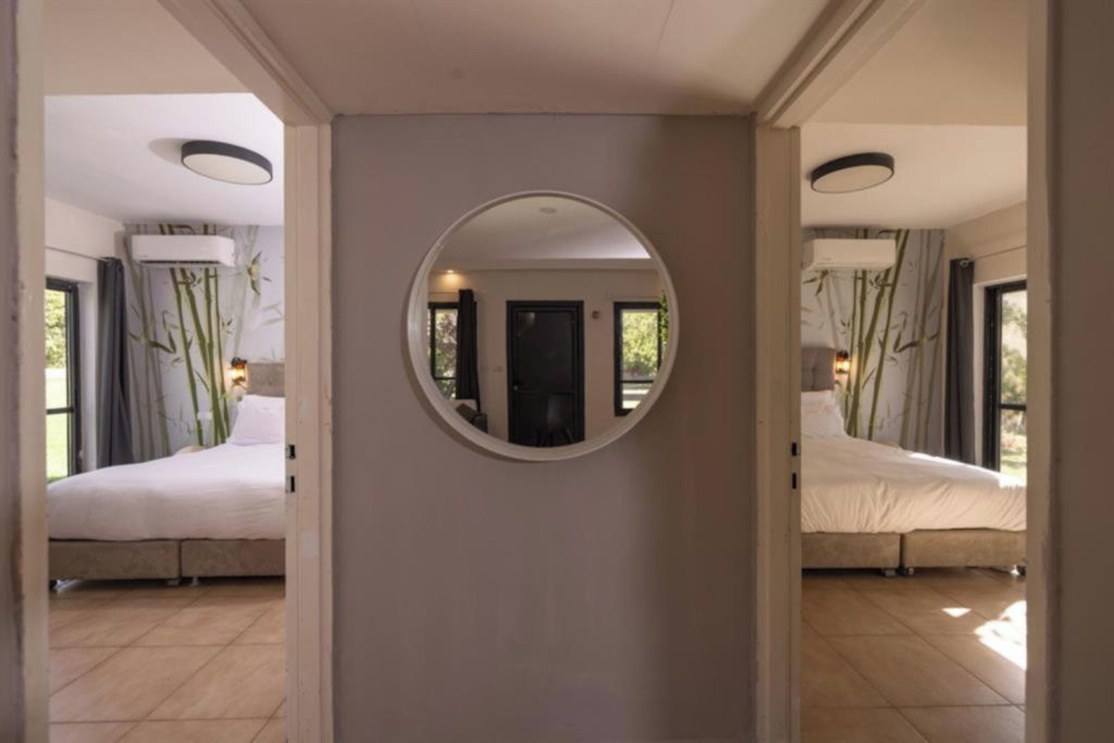 A hotel room with a large mirror, a bed, a door, and a view of the outside.