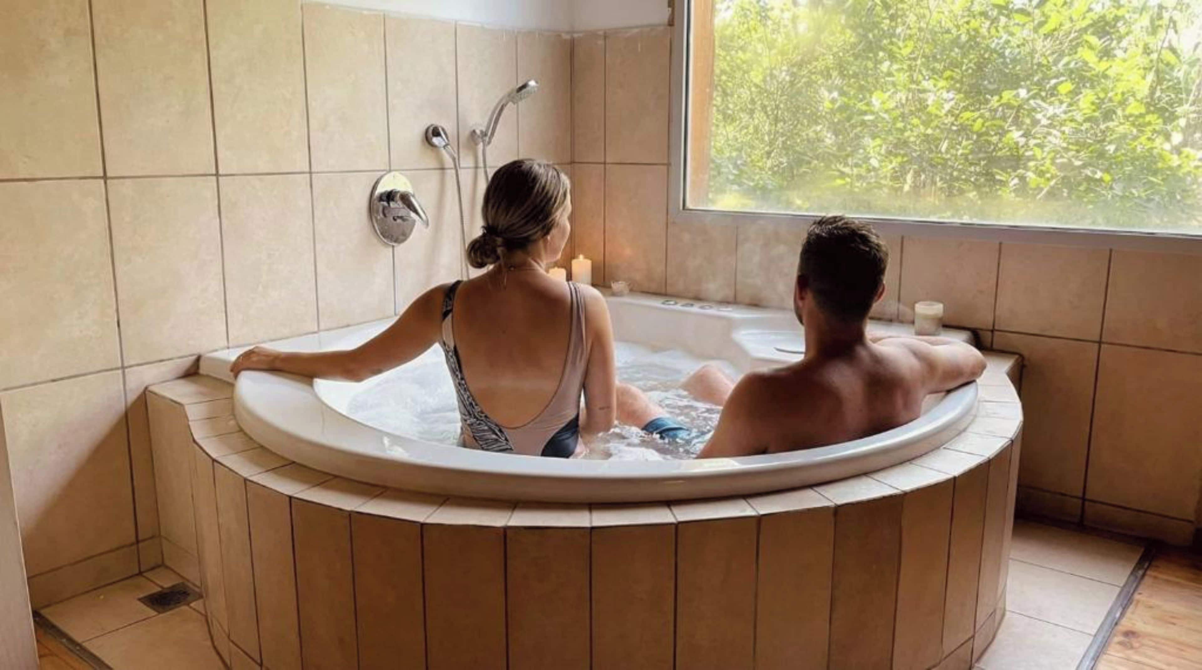 Una pareja en un jacuzzi con vistas a la vegetación.