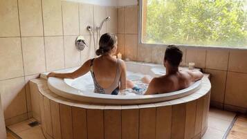 Una pareja en un jacuzzi con vistas a la vegetación.