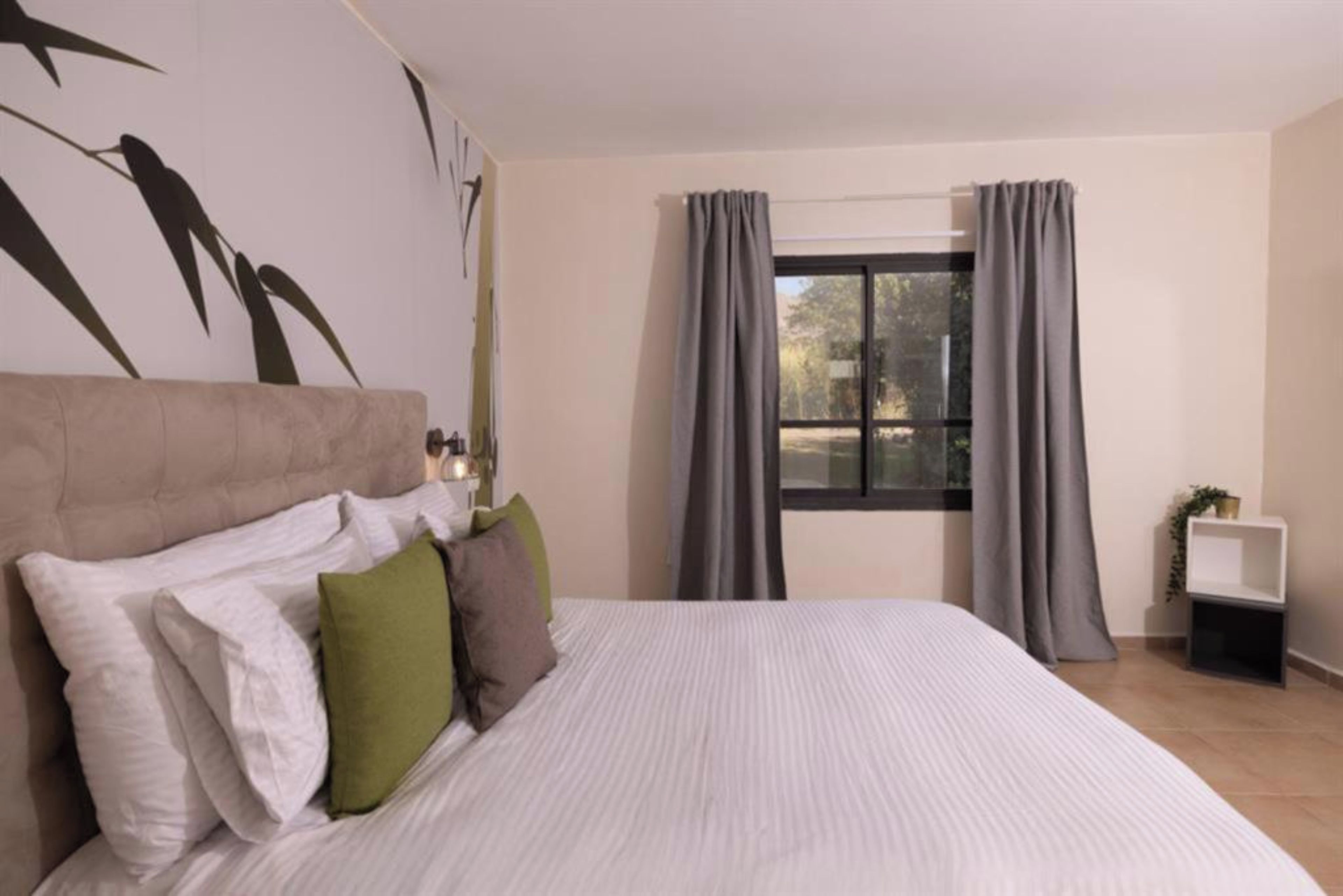Un dormitorio con una cama grande, un cabecero y una ventana con cortinas.