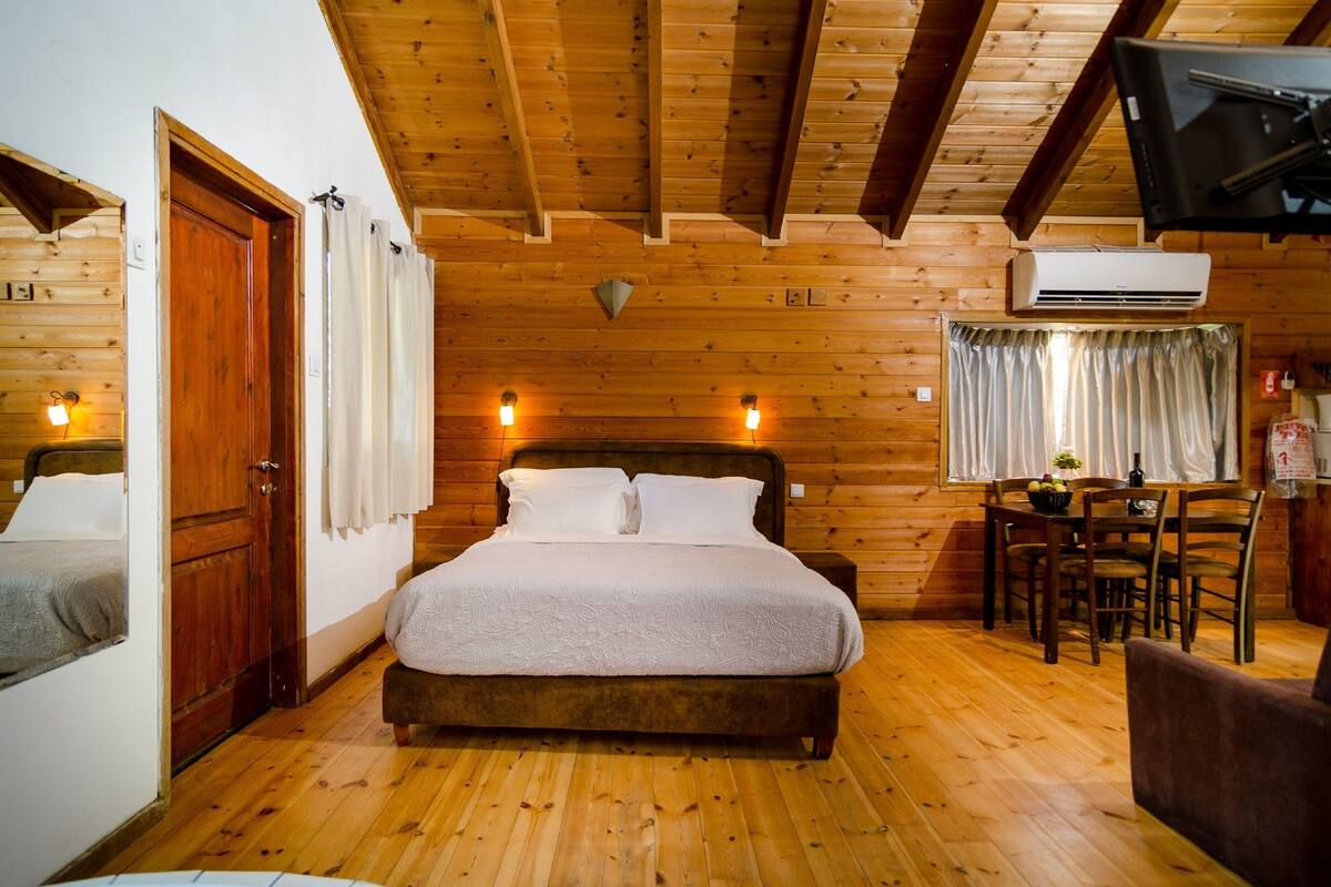 A wooden cabin room with a bed, a table, chairs, and an air conditioning unit.