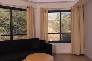 Una habitación con un sofá negro, una mesa redonda y ventanas con cortinas beige.