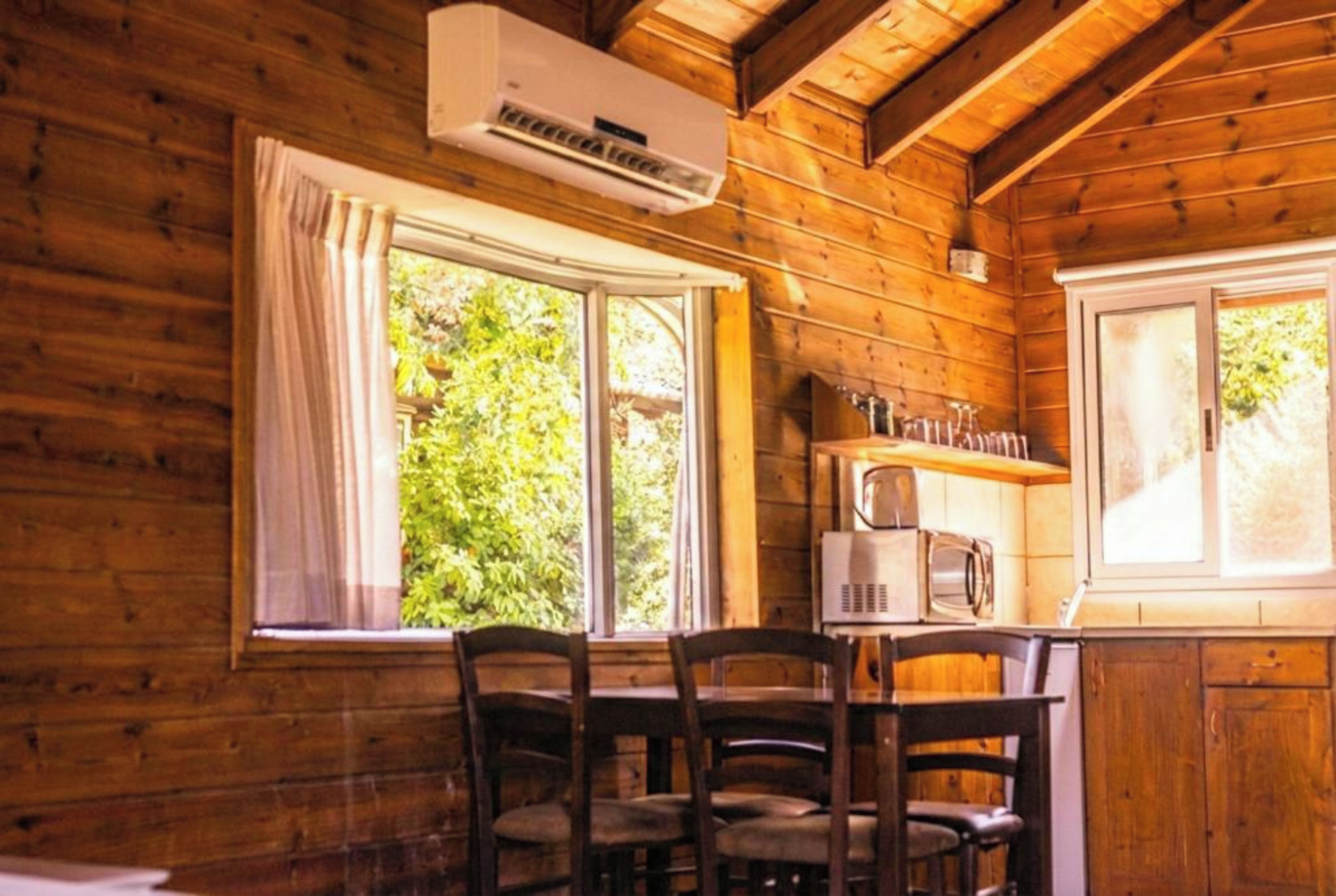 Interior de una cabaña de madera con una mesa de comedor, sillas, microondas y aire acondicionado.