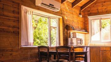 Interior de una cabaña de madera con una mesa de comedor, sillas, microondas y aire acondicionado.