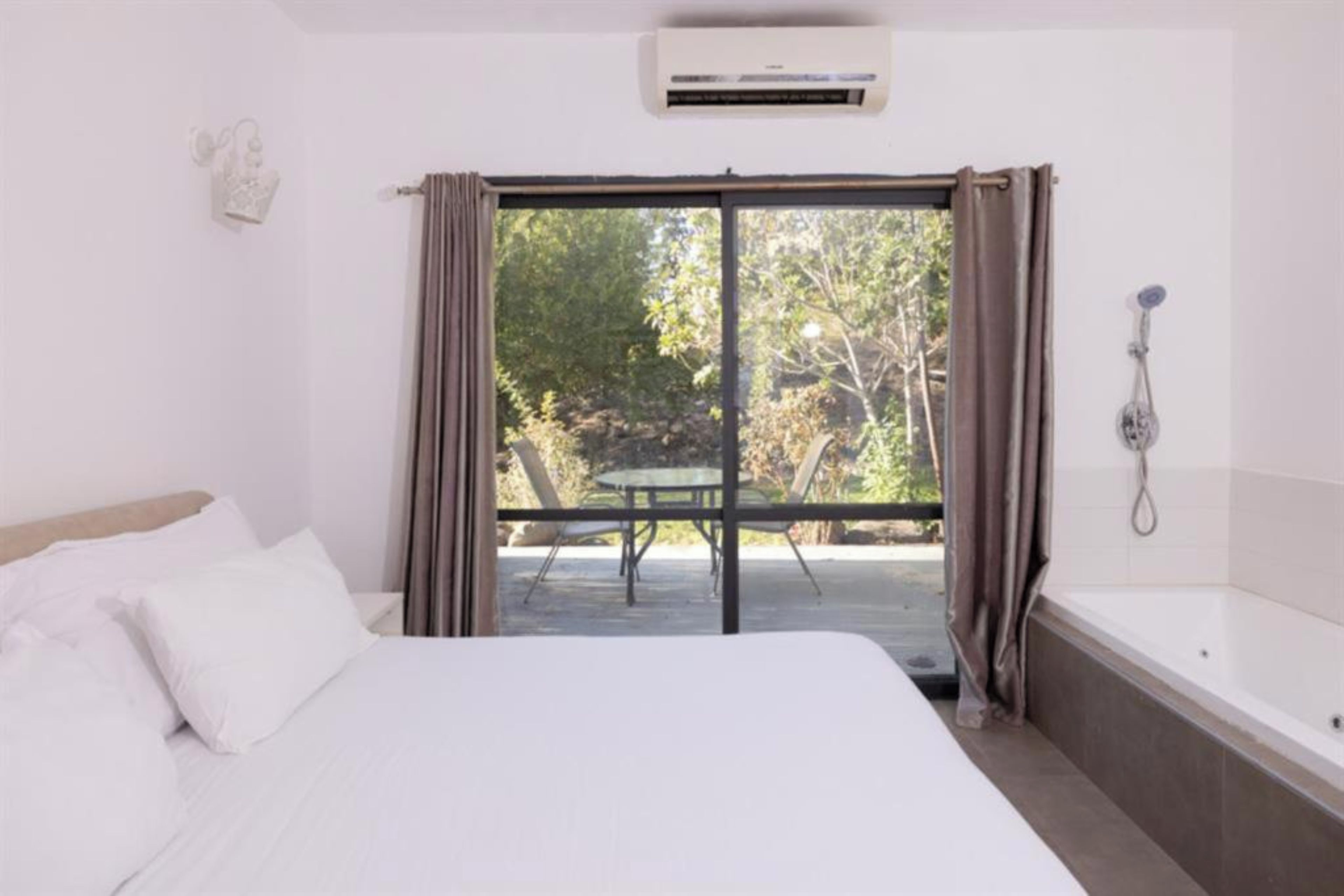 Una habitación de hotel con cama, ducha y balcón con mesa y sillas.
