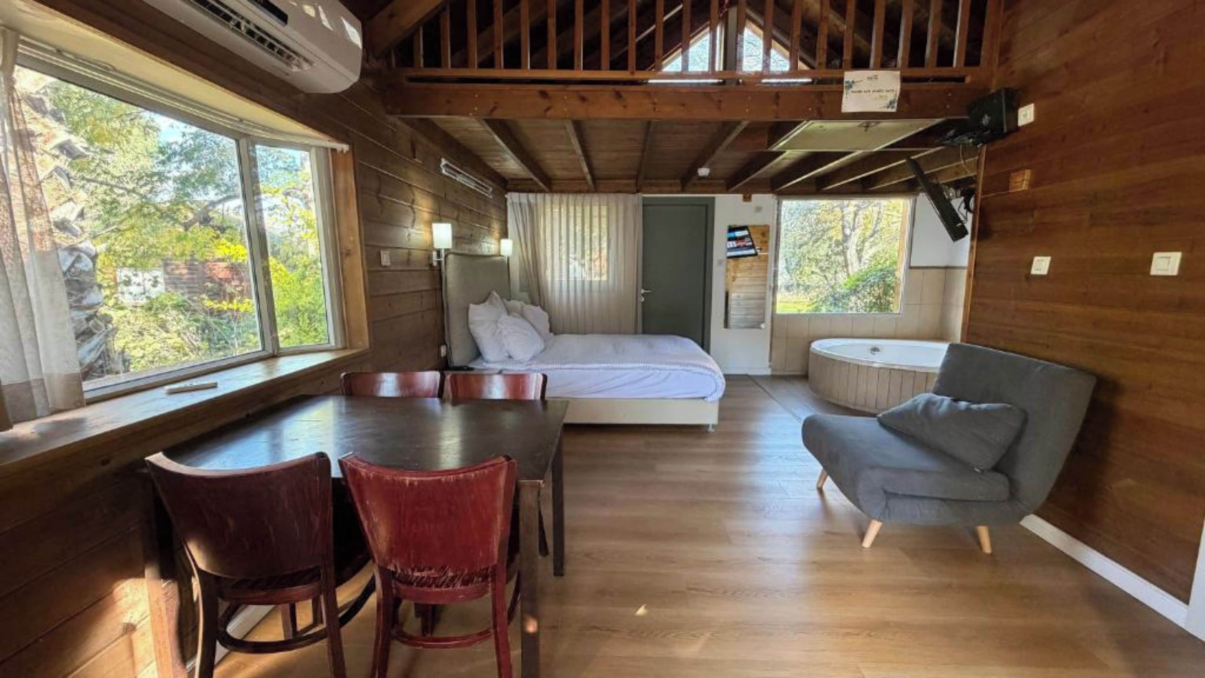 Interno di una baita con pavimento in legno, un letto, un tavolo da pranzo con sedie e un piccolo divano.
