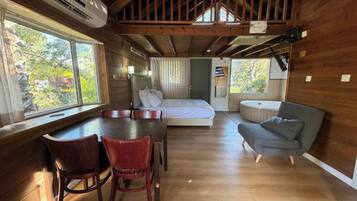Interno di una baita con pavimento in legno, un letto, un tavolo da pranzo con sedie e un piccolo divano.