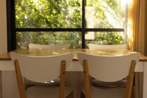 A dining table with two chairs, a window with a view of greenery, and a curtain on the right. - Nofey Habashan Country Lodge (HaGalil HaElyon)