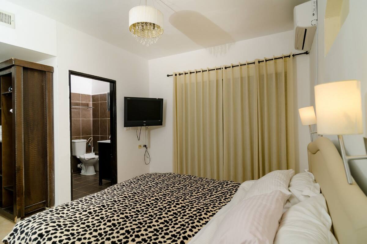 A hotel room with a bed, a television, a bathroom with a shower, and a curtain.